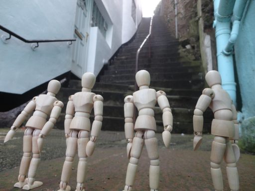 Four wooden artist mannequins stand at the base of a long, steep staircase.